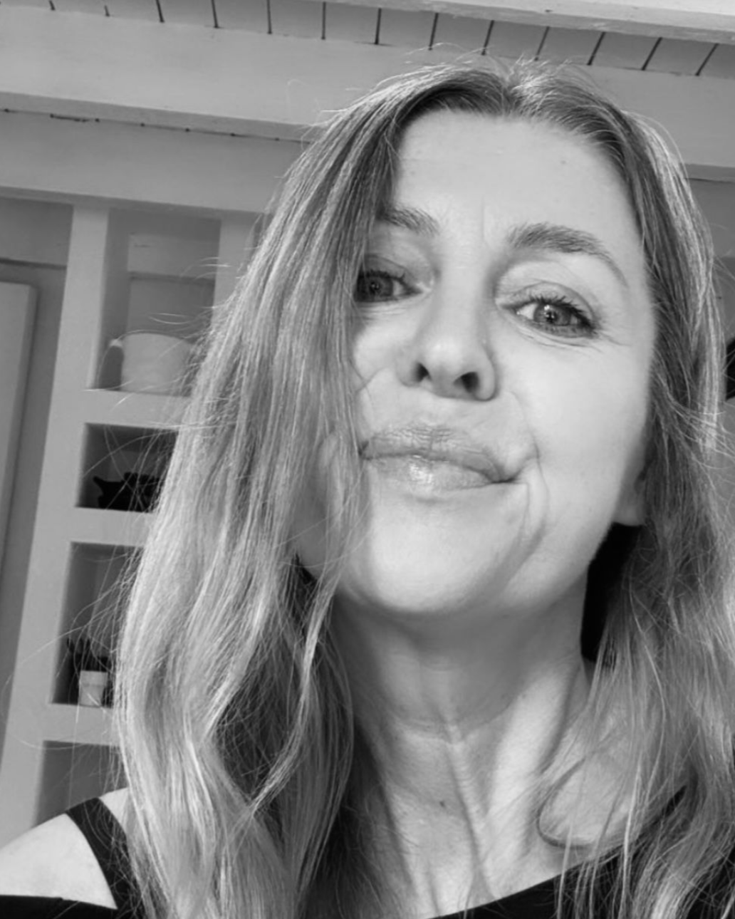 Vrouw met lang haar kijkt met een lichte glimlach in de camera. Zwart-witfoto.