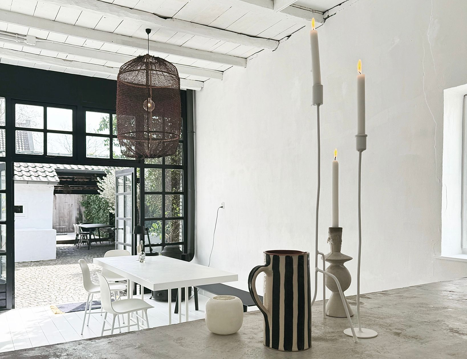 Lichte, moderne eetruimte met witte muren, uitzicht op een patio en decoratieve kaarsen.