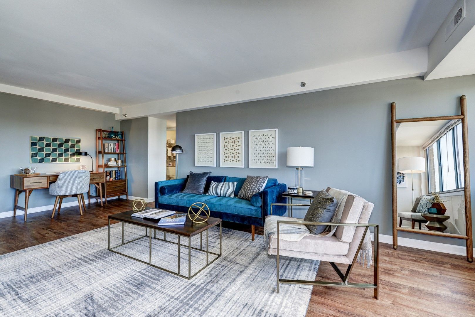A living room with a blue couch , chairs , a coffee table, and a mirror at The Mark by Solaire Apartments for rent in Alexandria, VA.