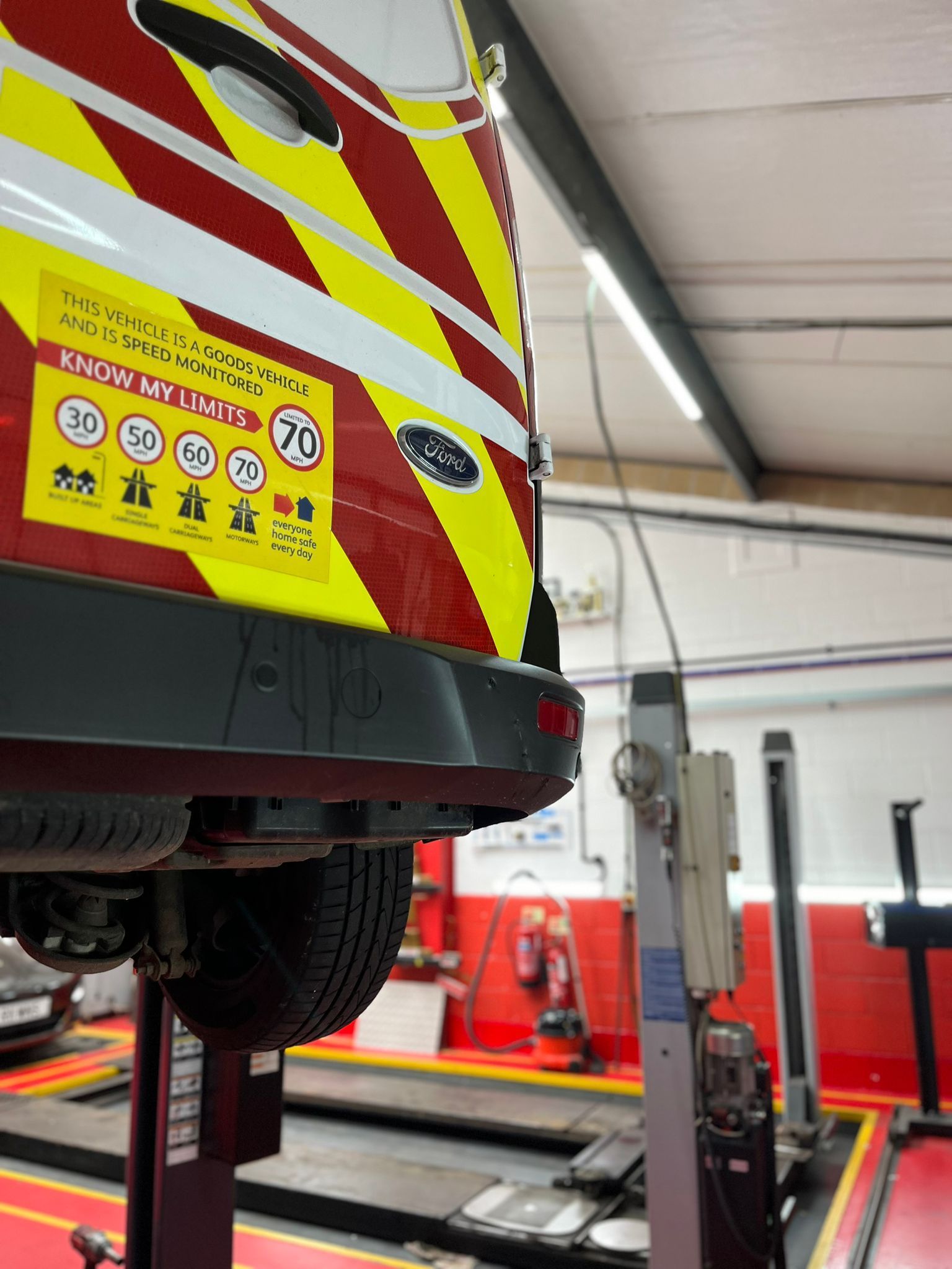 A red and yellow van is on a lift in a garage