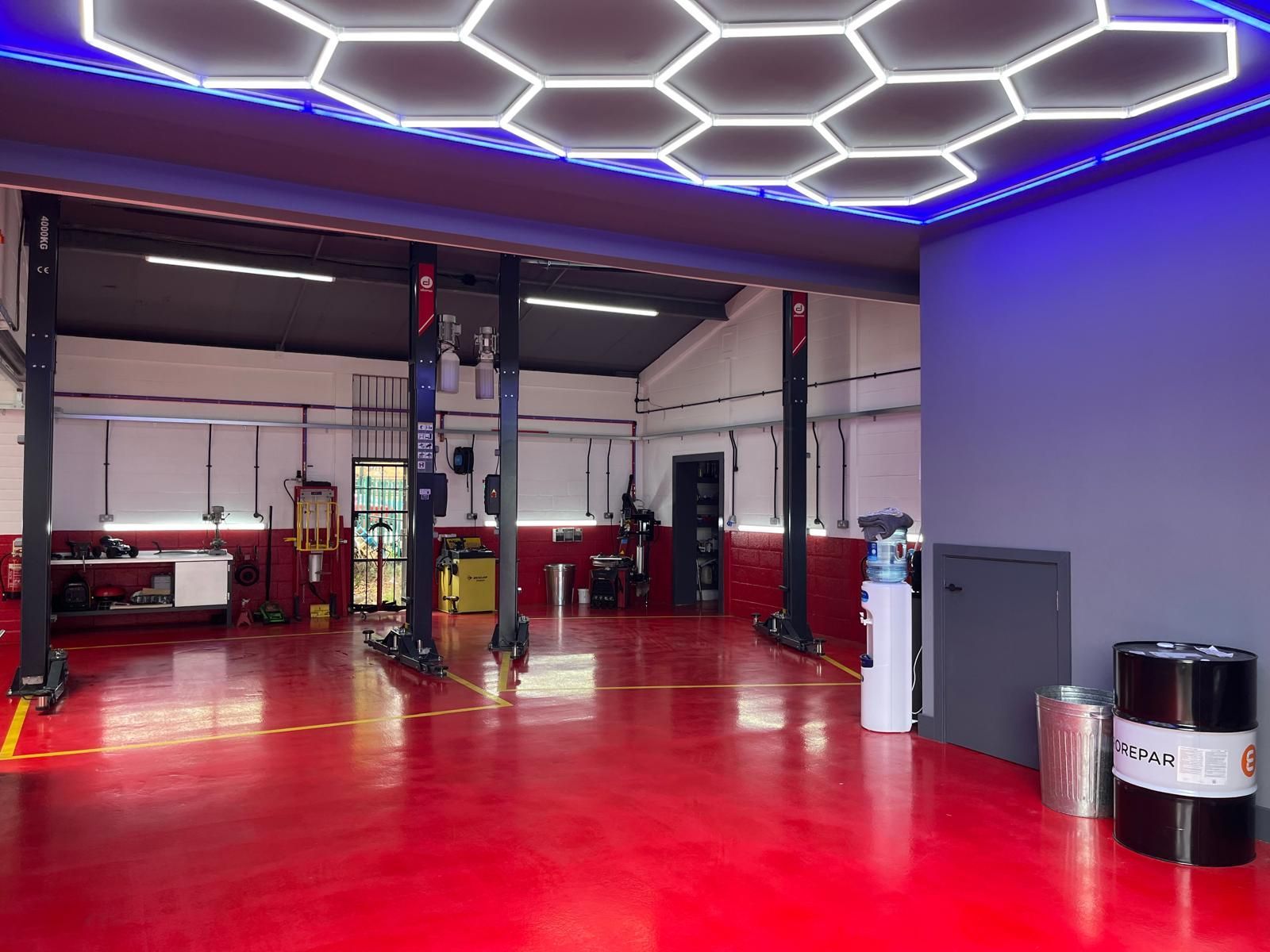 A large empty garage with a red floor and a honeycomb ceiling.