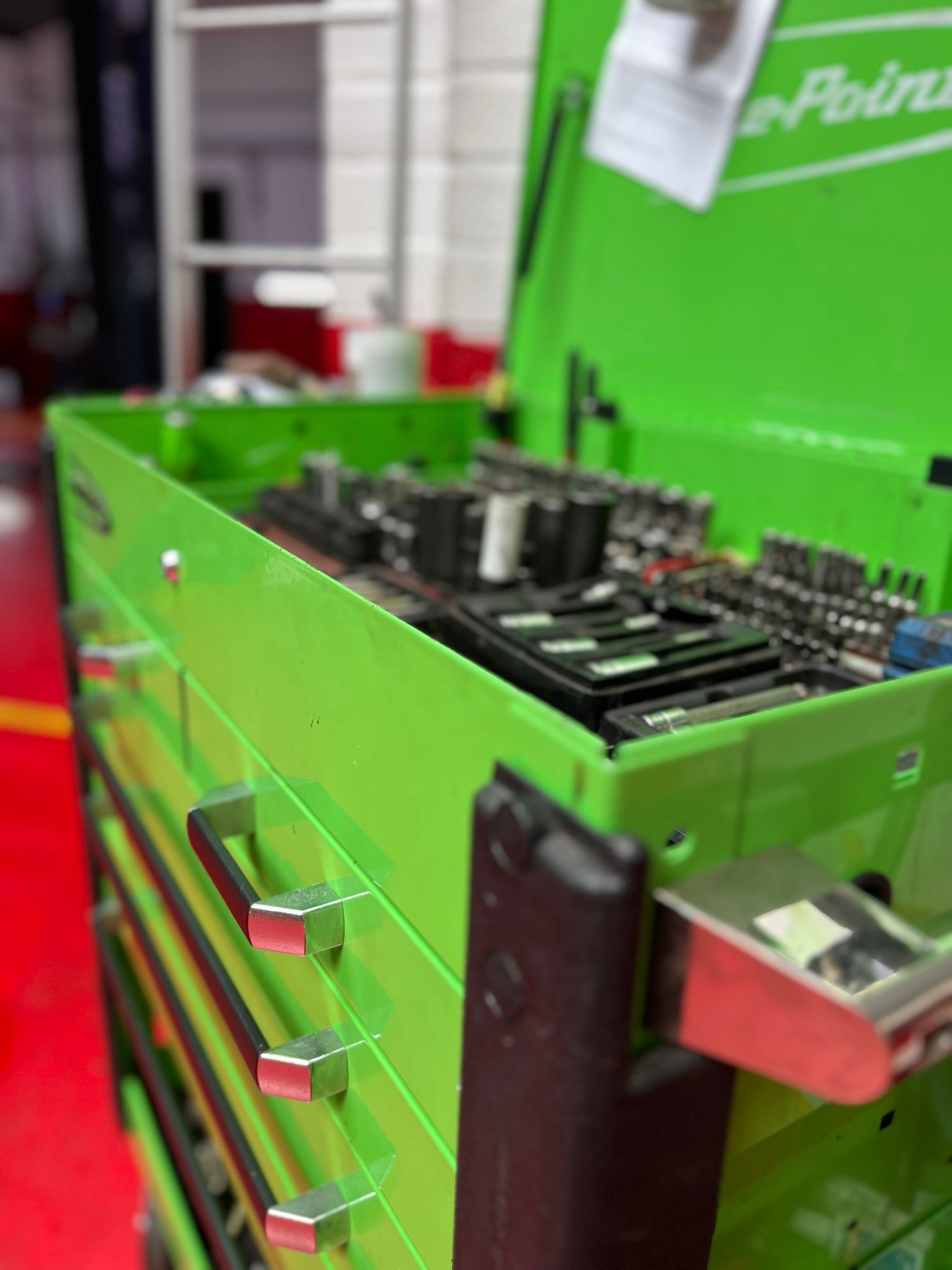 A green toolbox filled with tools is sitting on top of a red table.