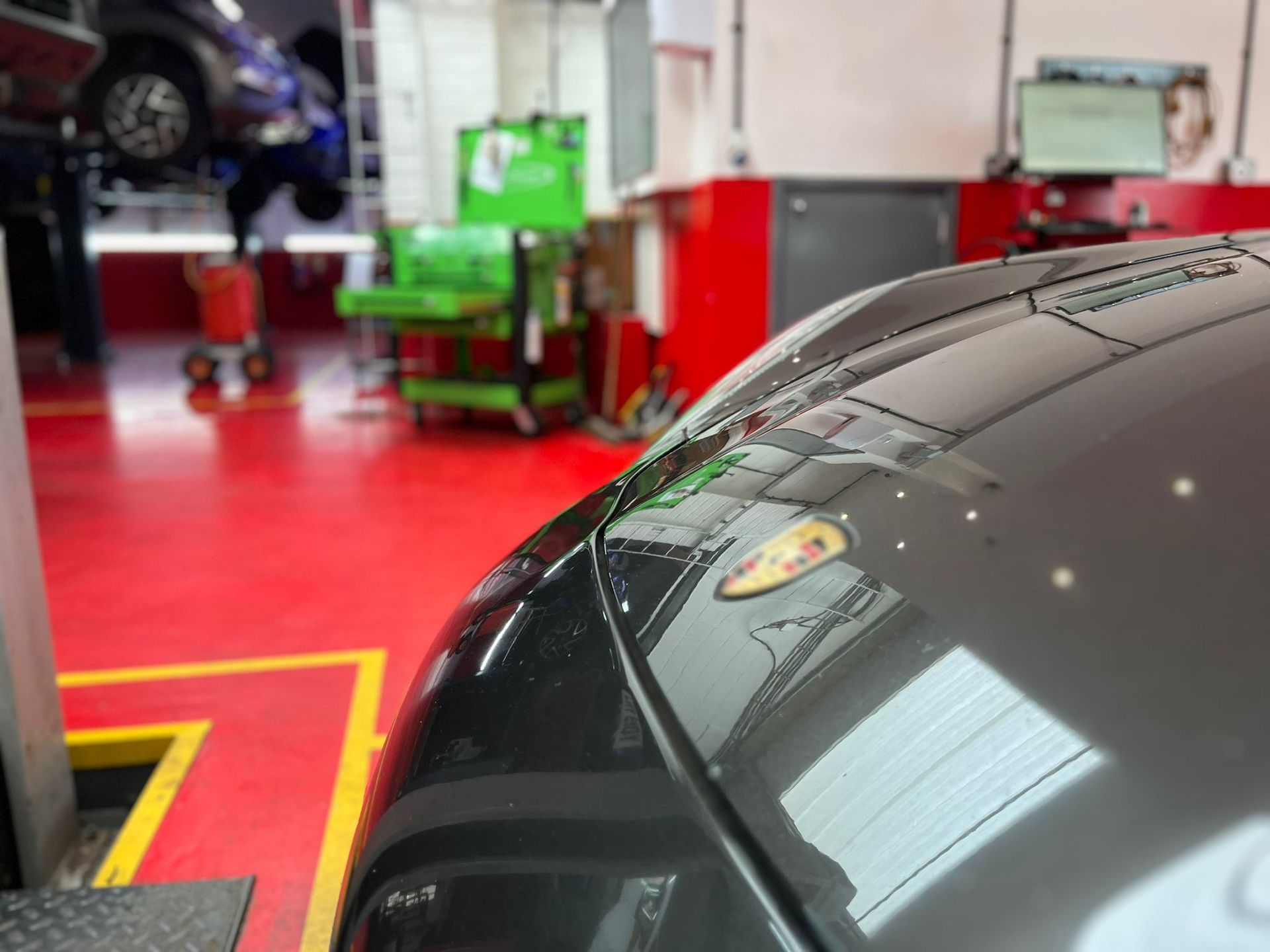 A black car is parked in a garage with a red floor.