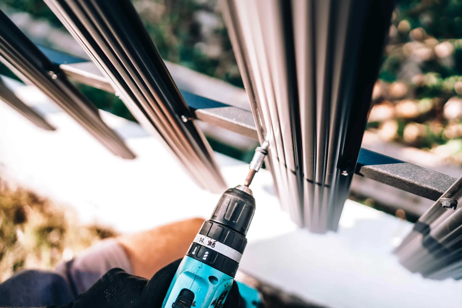 Close-up of a blue power drill tightening a metal railing bolt near a snowy drop-off