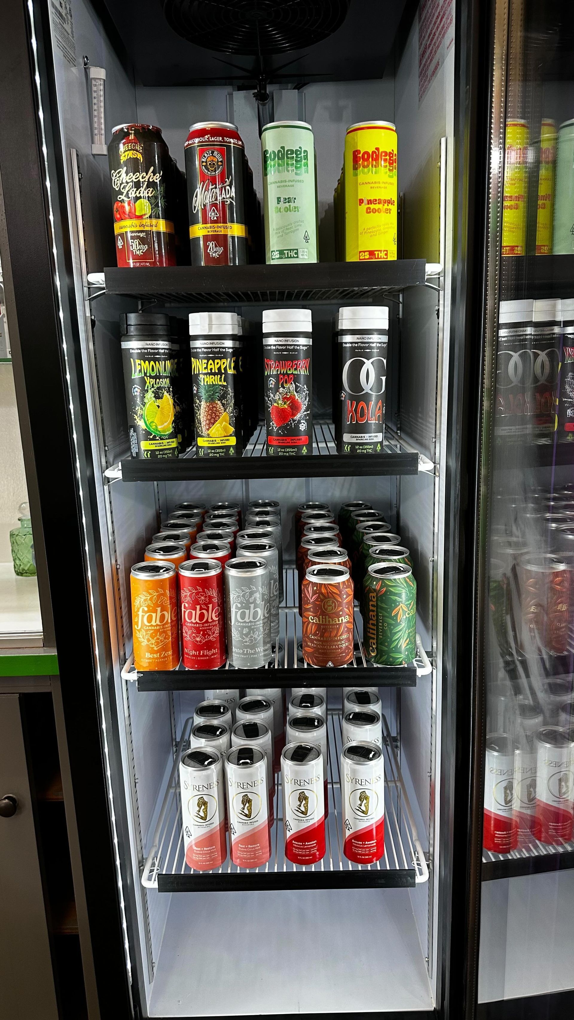 A refrigerator display case filled with rows of assorted energy drink cans on four glass shelves.