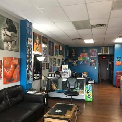A tattoo studio with artwork displayed on blue and white walls, a black couch, a reception desk, and a rolling chair.