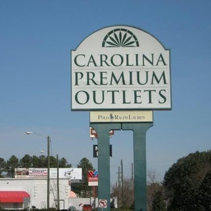 A large sign for Carolina Premium Outlets with a smaller Polo Ralph Lauren logo, set against a clear blue sky.