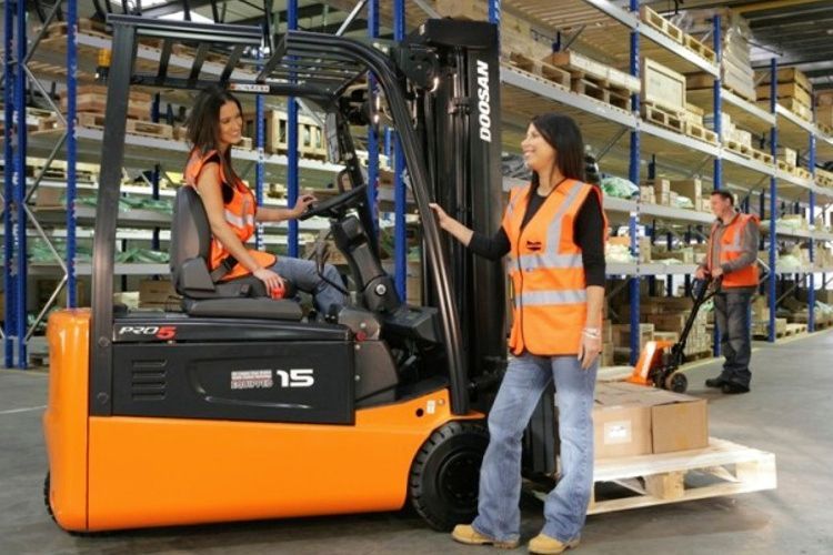 Two women talking around a forklift