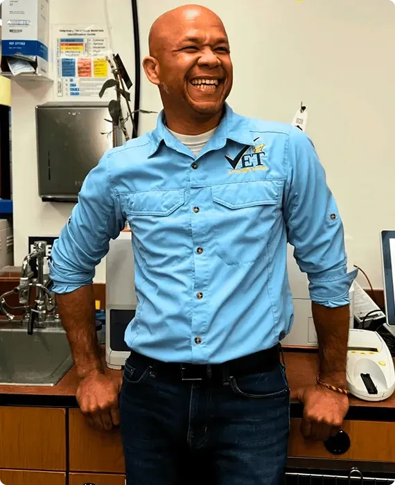 Smiling man in a light blue shirt leaning on a counter in a lab or office setting