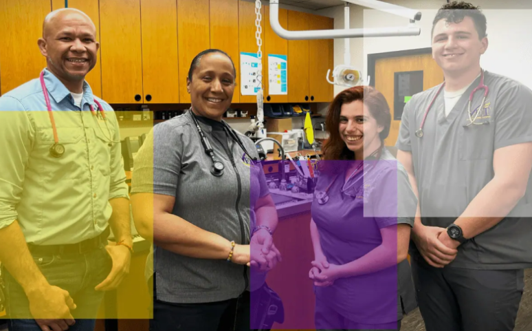 Four smiling lab staff stand together in a bright workshop, wearing lanyards and casual work clothes.