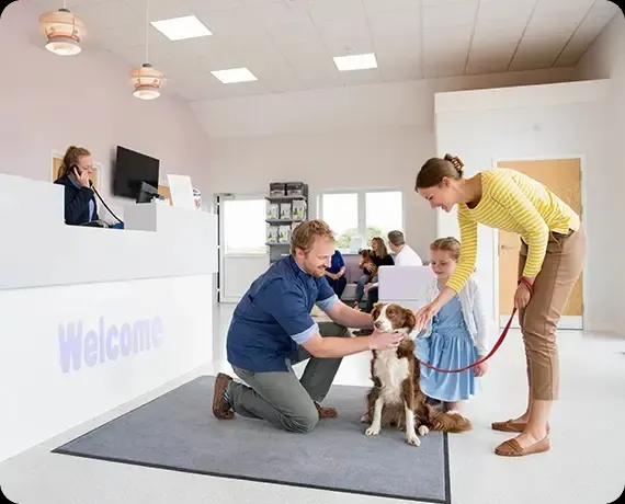 Veterinarian kneels to pet a dog while a woman and child watch in a bright clinic lobby