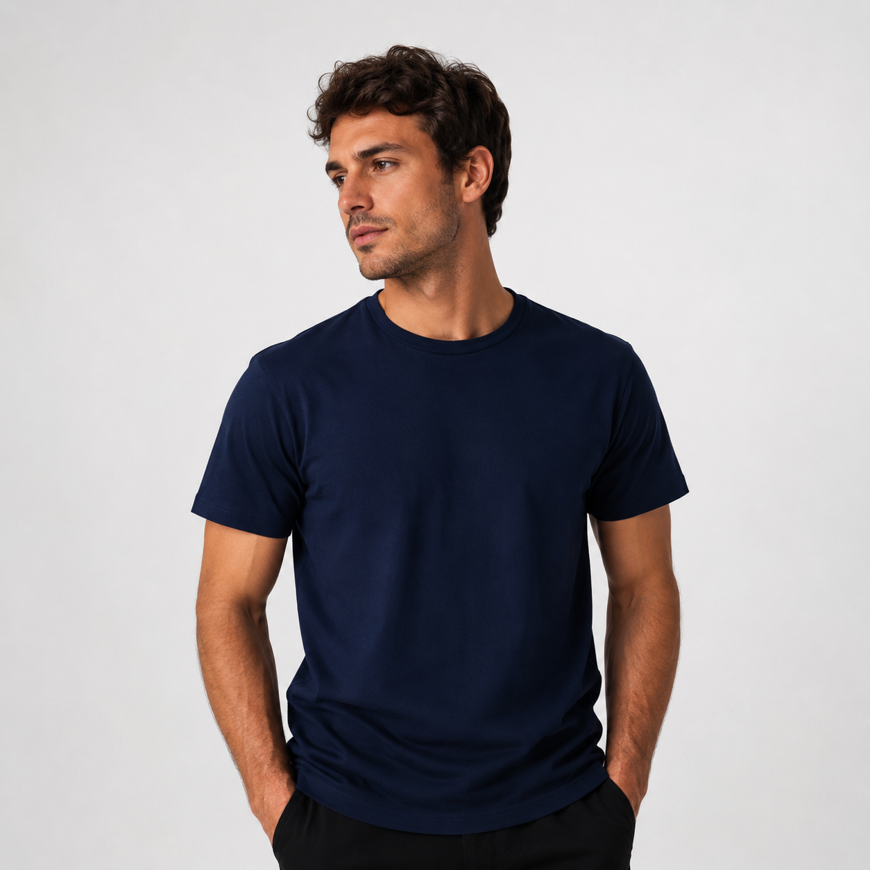 Hombre con camiseta azul marino posando frente a un fondo claro liso, mirando hacia un lado.