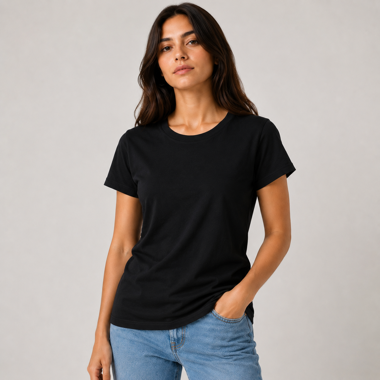 Mujer con camiseta negra y vaqueros azul claro posando sobre un fondo gris claro.