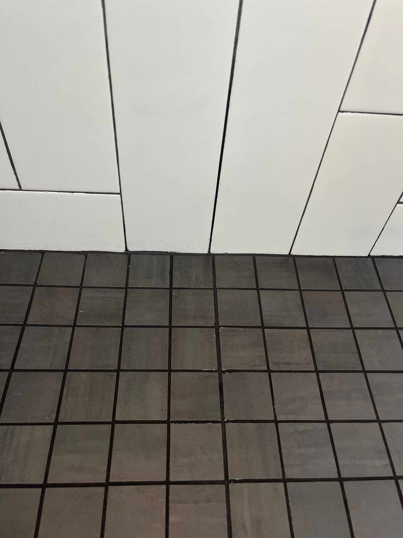 White tiled wall above dark gray grid-pattern floor tiles.