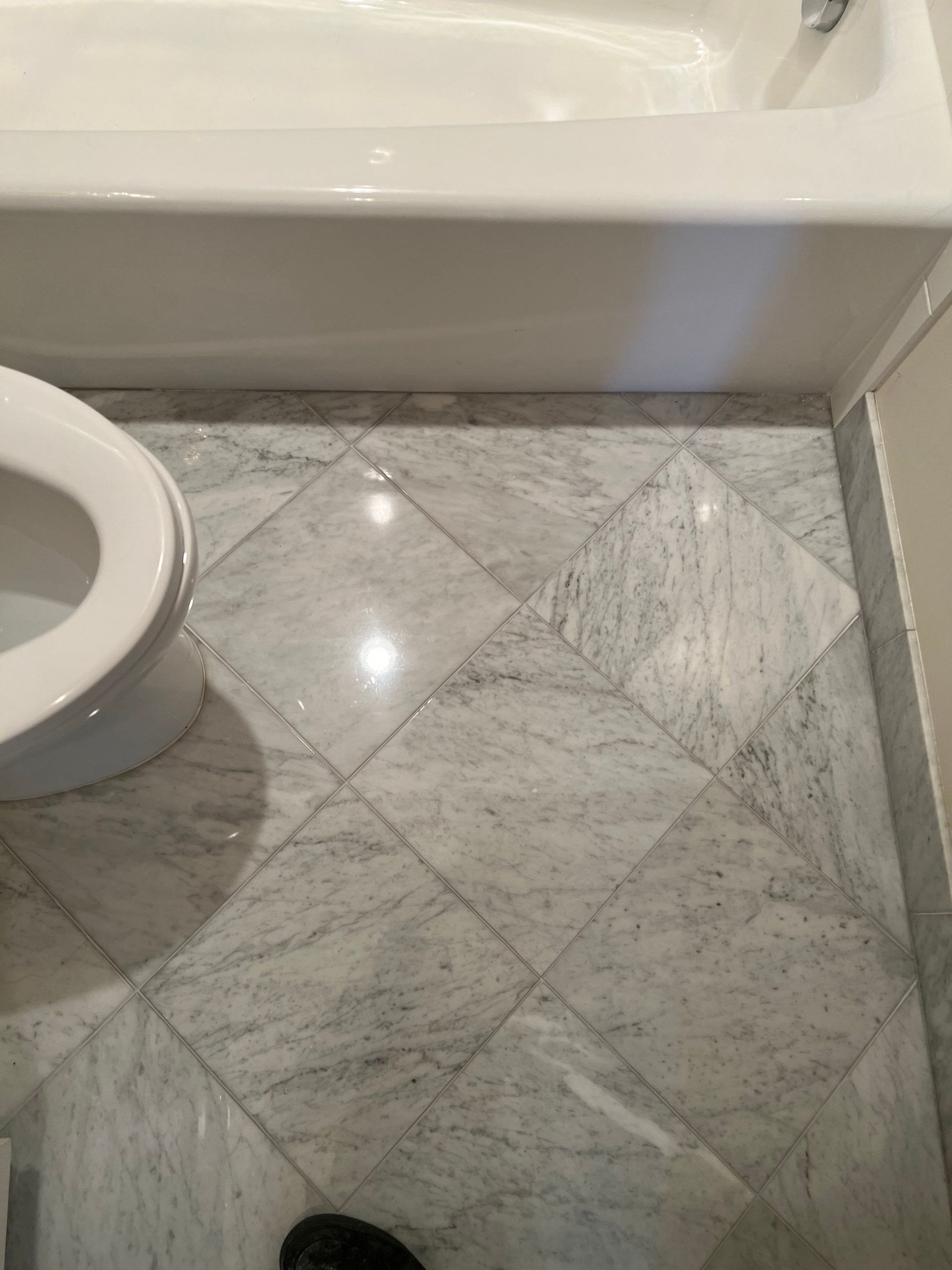 Bathroom floor with gray marble tiles beside a white bathtub and toilet.