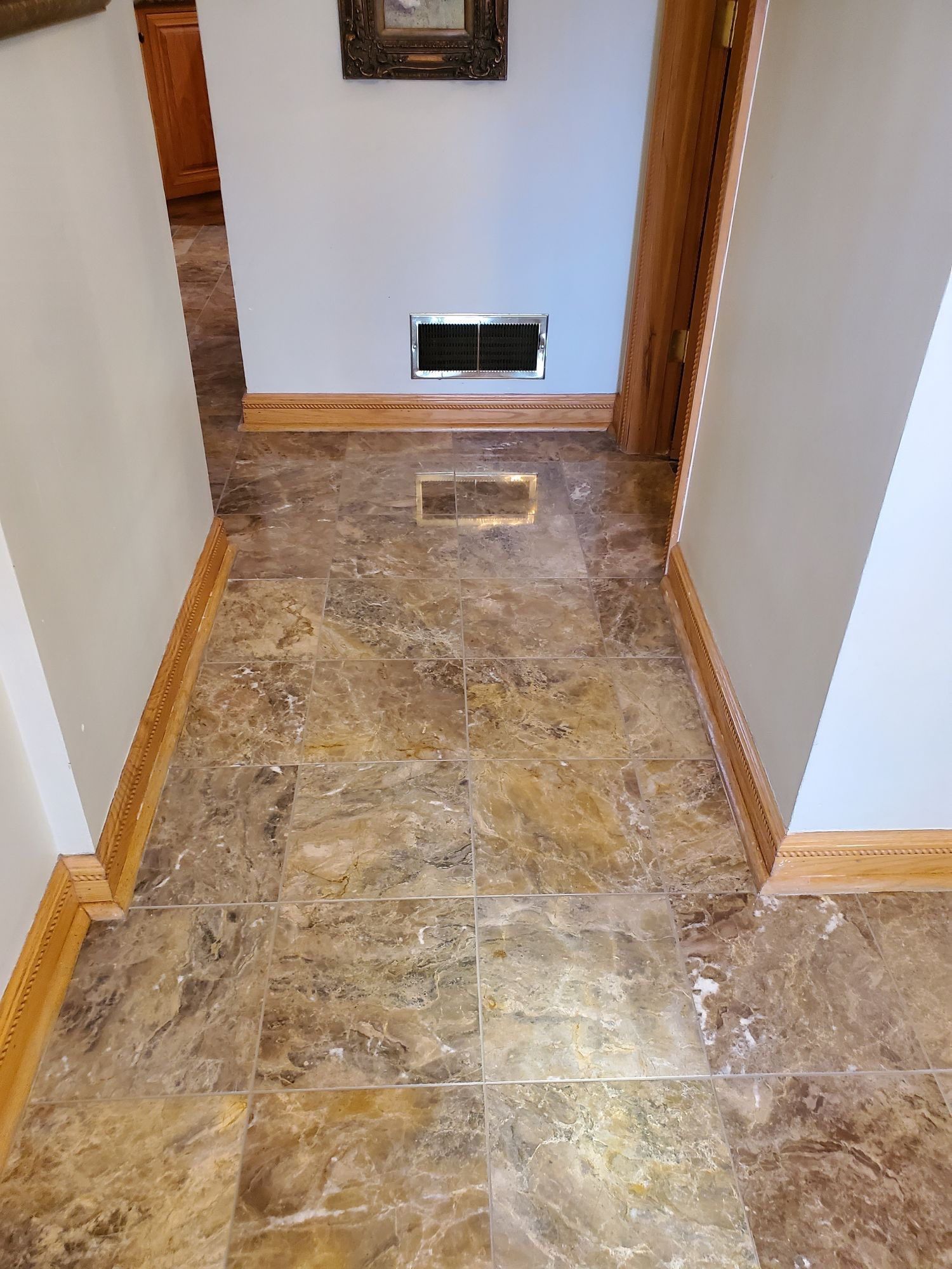 Narrow hallway with marble tile floor, white walls, wood trim, and a wall vent at the end.