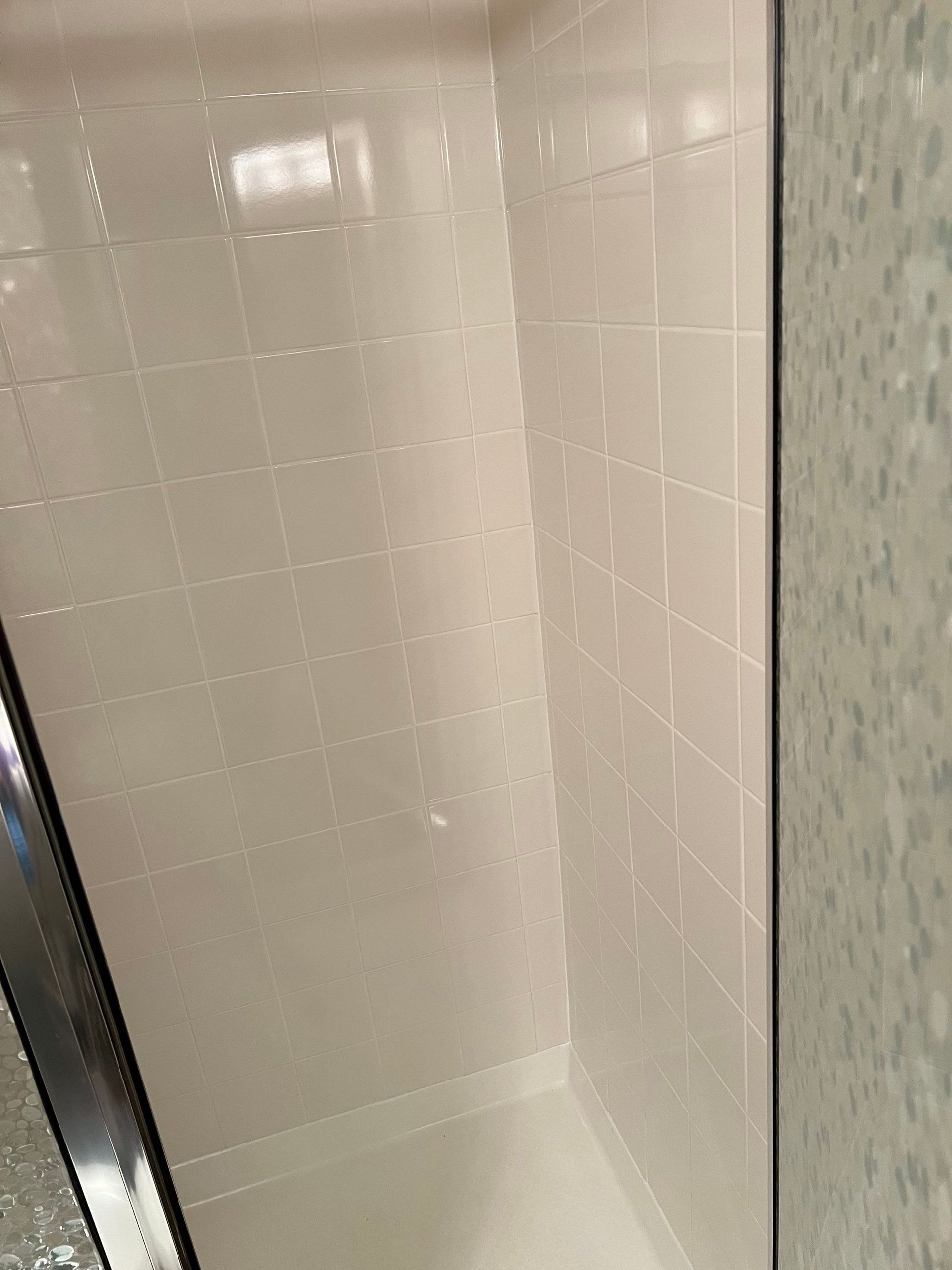 Small white tiled shower stall with a glass door and chrome trim