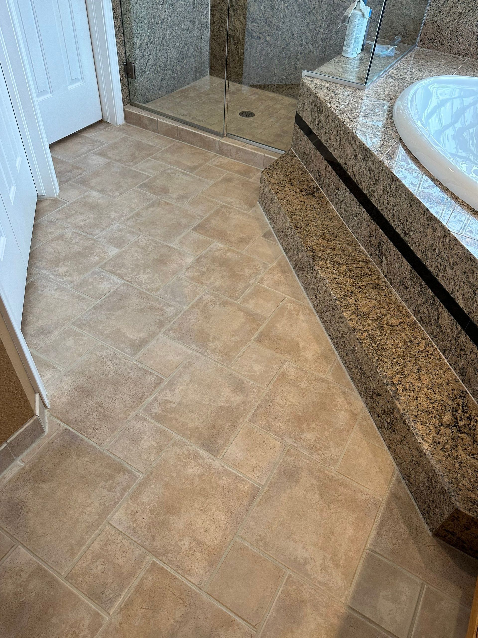 Bathroom floor with beige tile, glass shower door, and granite vanity edge