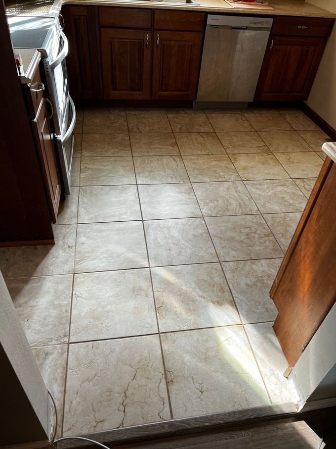Kitchen with beige tiled floor, wooden cabinets, and a stainless steel dishwasher beside a sunlit doorway