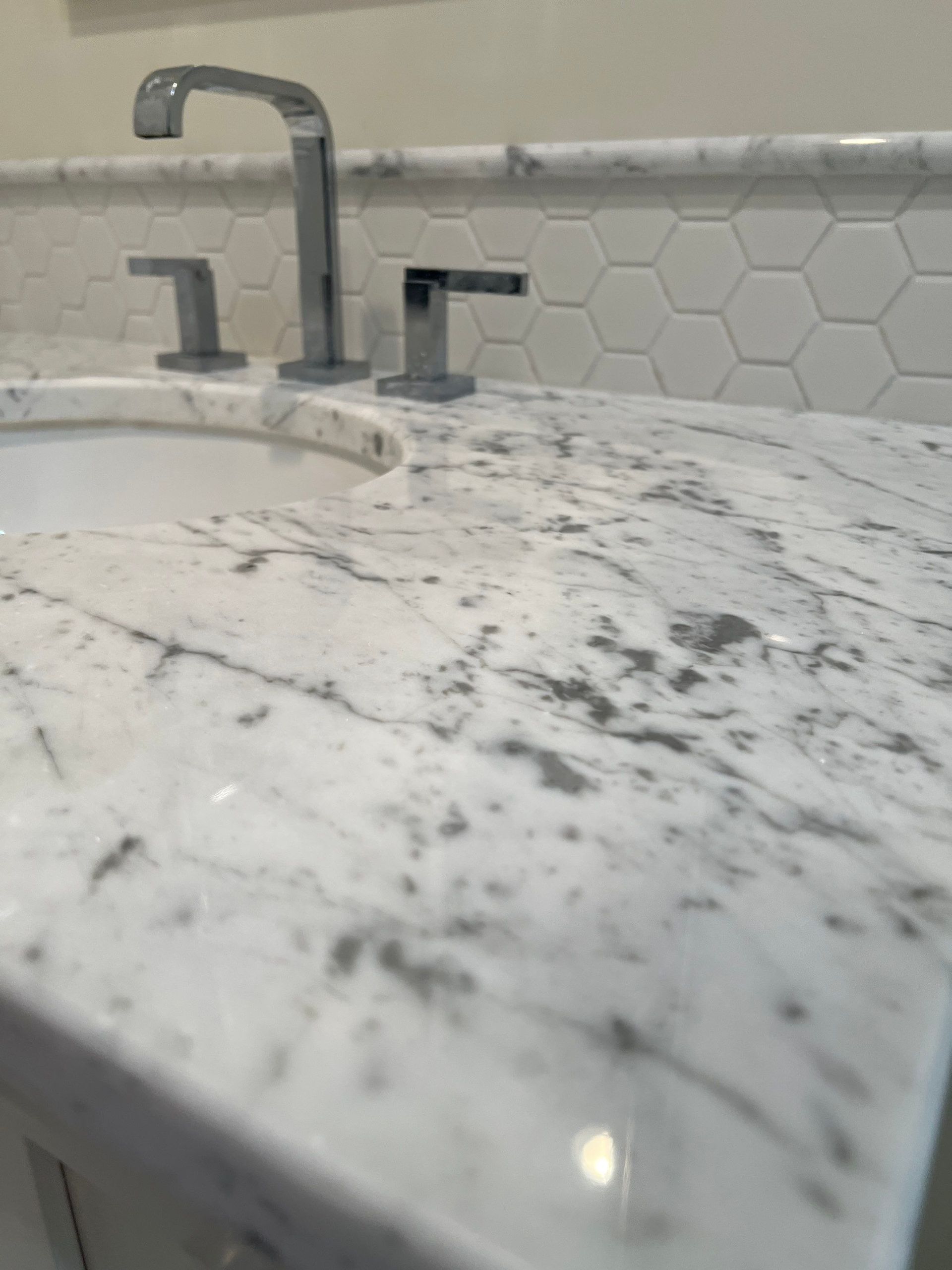 Bathroom sink with silver faucet, marble countertop, and white hexagon tile backsplash.