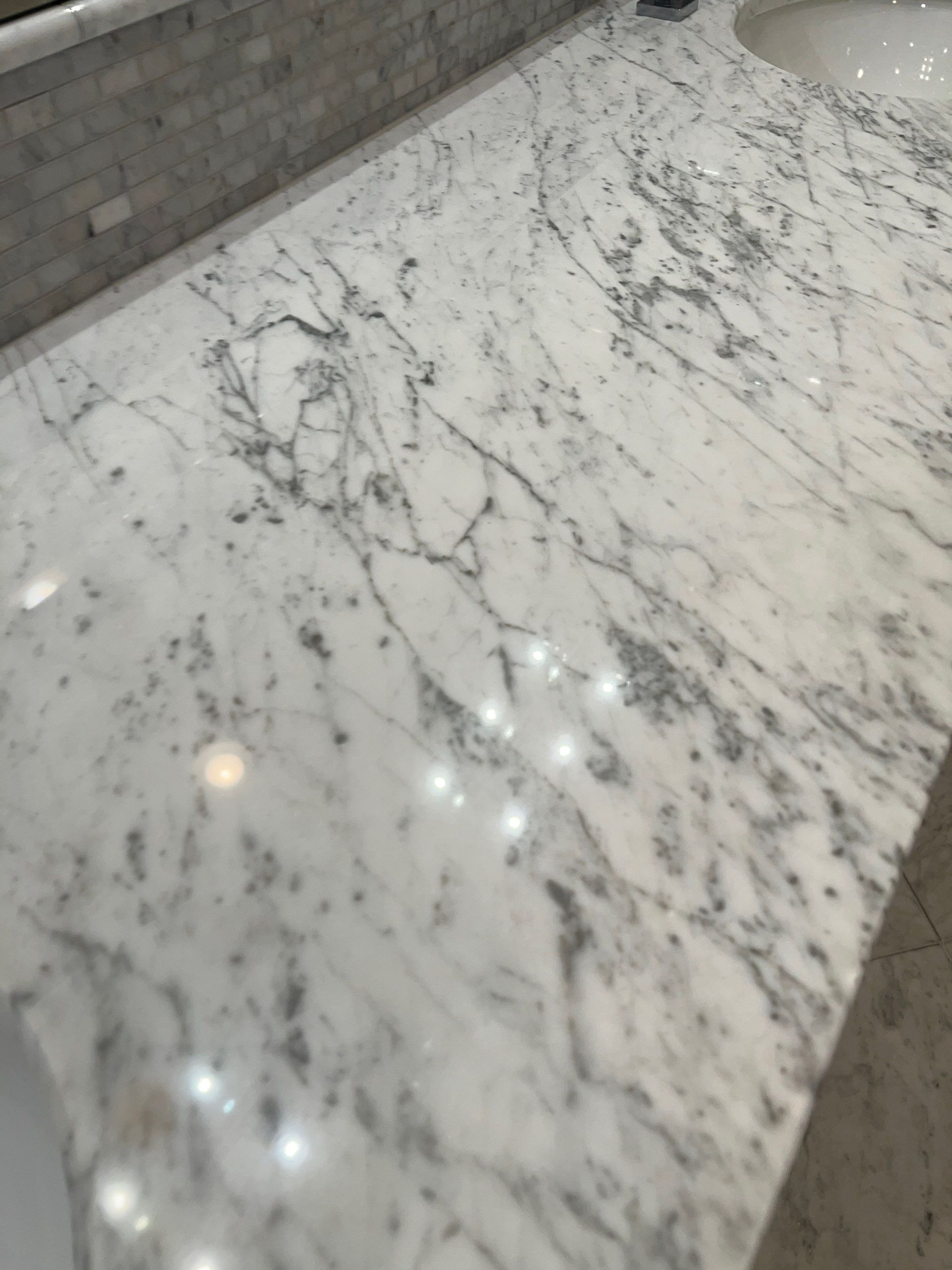 White marble countertop with gray veining and reflective lights beside a tiled backsplash