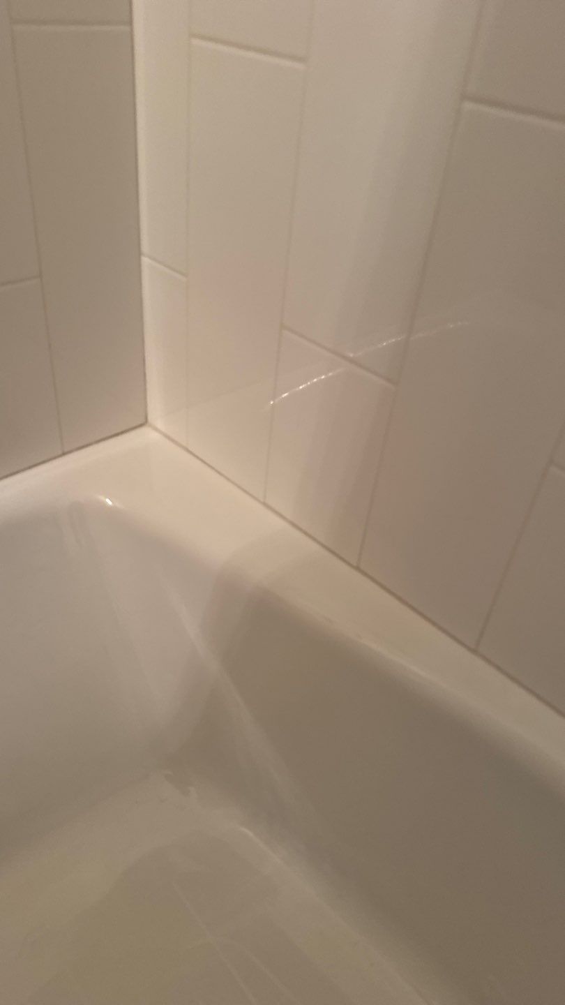 White bathtub corner with glossy white tiled shower wall and grout lines
