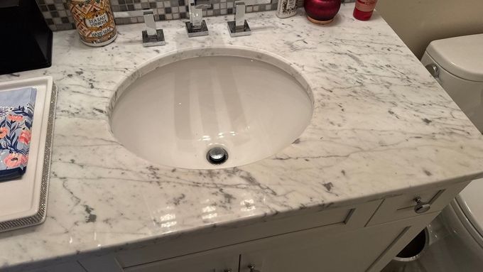 Marble bathroom vanity with a white sink and countertop items, including a tissue box and small containers