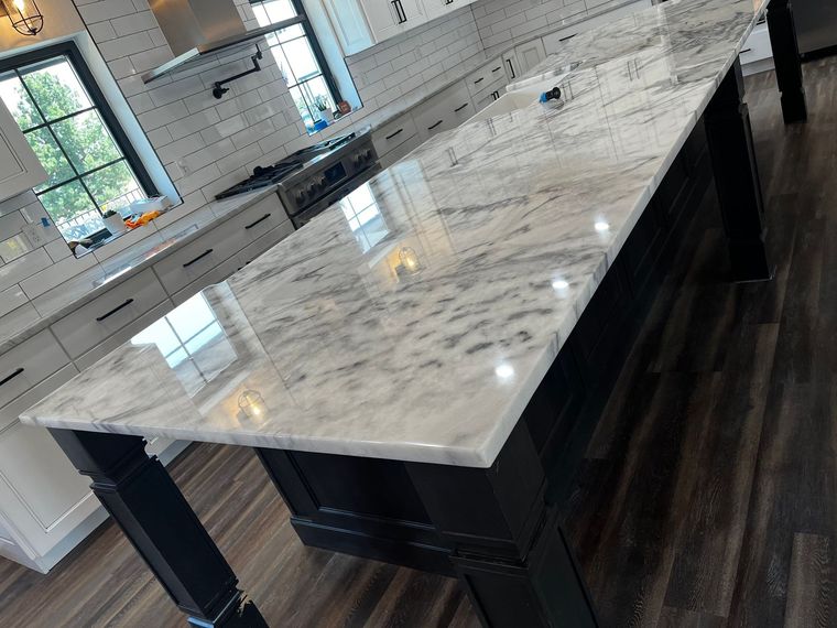 Large white marble kitchen island with dark base in a bright modern kitchen