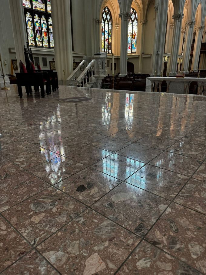 Marble church floor reflecting stained-glass windows and pews in a bright sanctuary