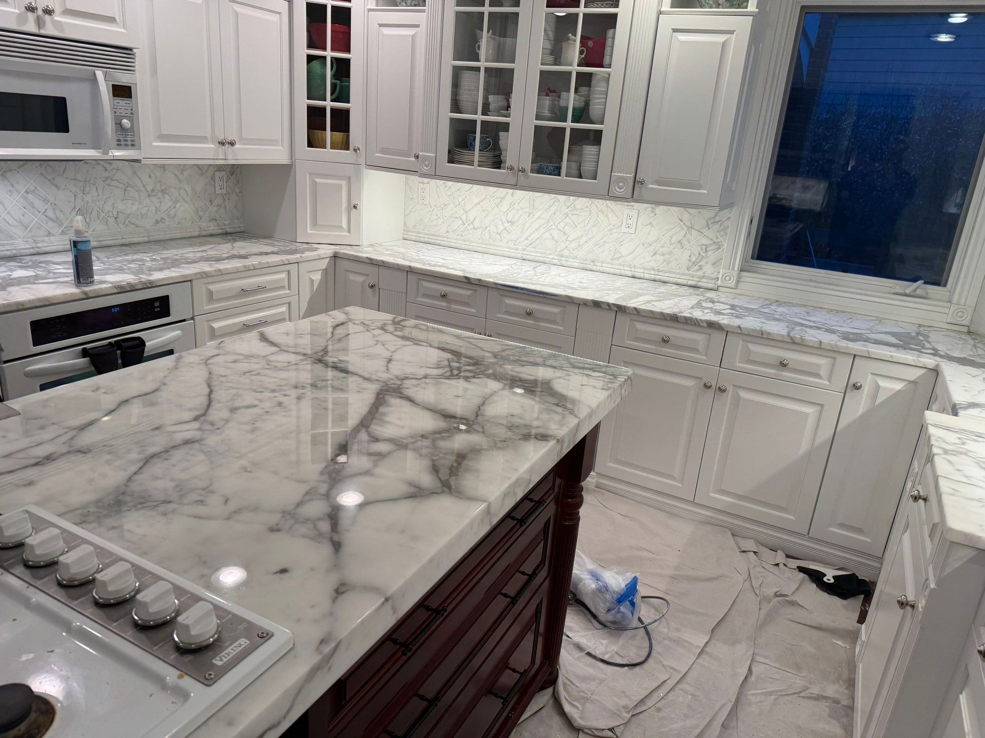 Modern white kitchen with marble island, stainless appliances, and cabinets with glass doors