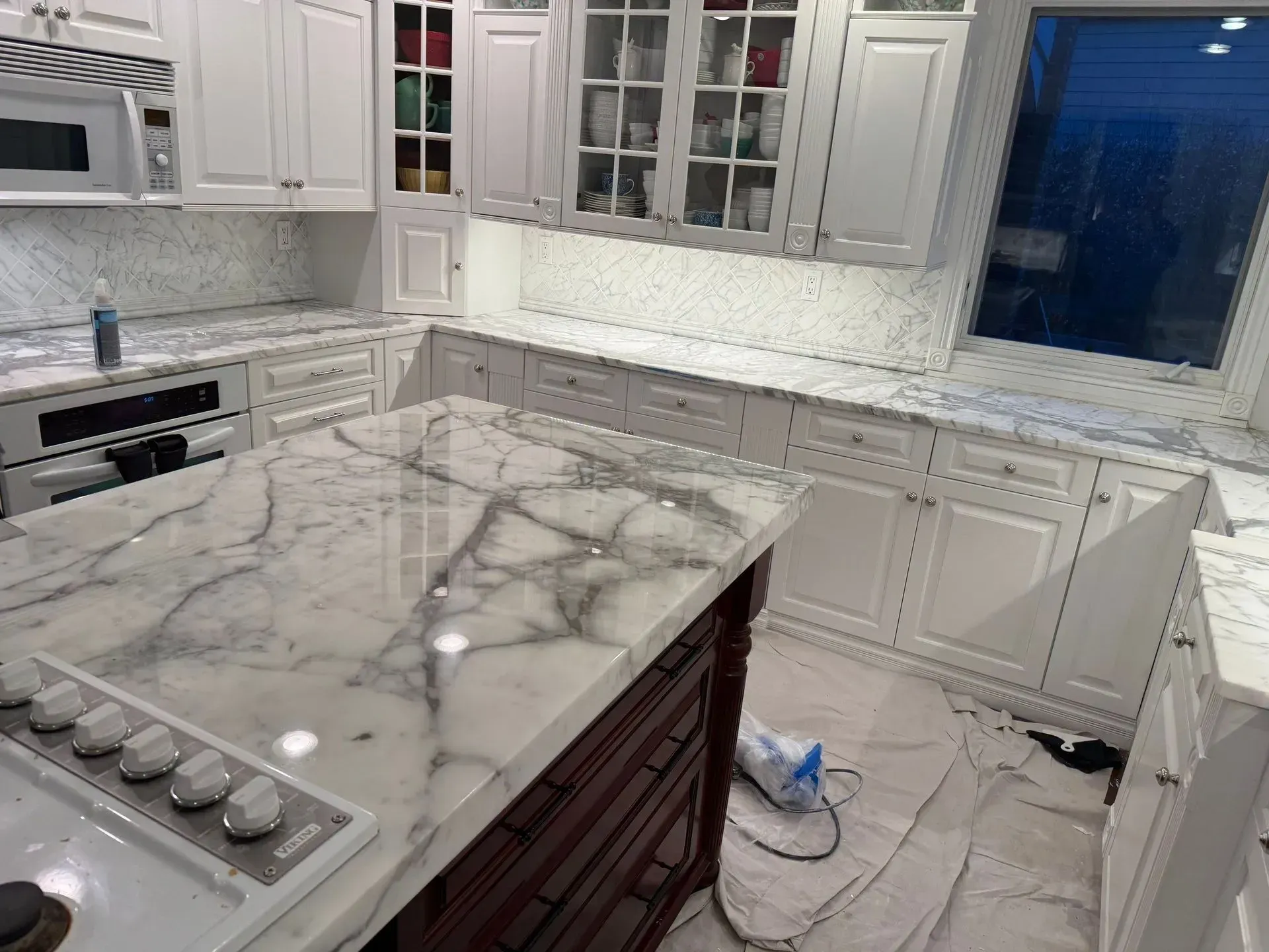 Modern kitchen with white cabinets, marble island, stainless appliances, and a dark window on the right