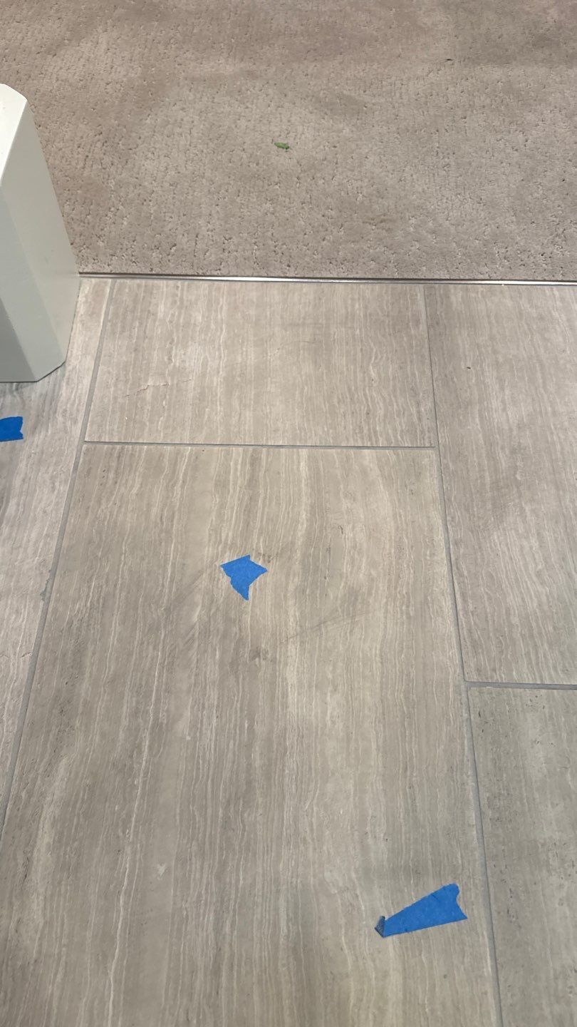 Gray carpet and tile flooring with blue tape markers near a doorway