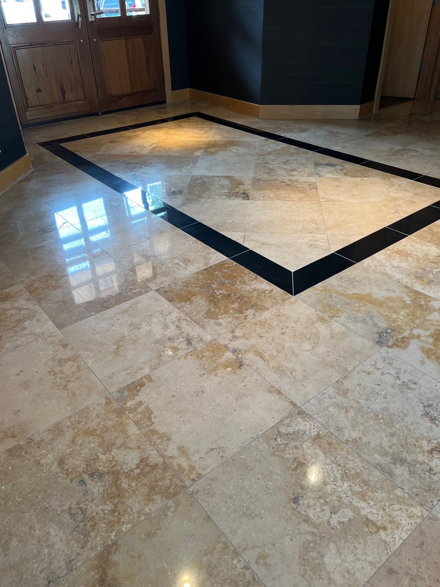 Marble lobby floor with a dark inlaid border and sunlight reflecting from a window near wooden doors