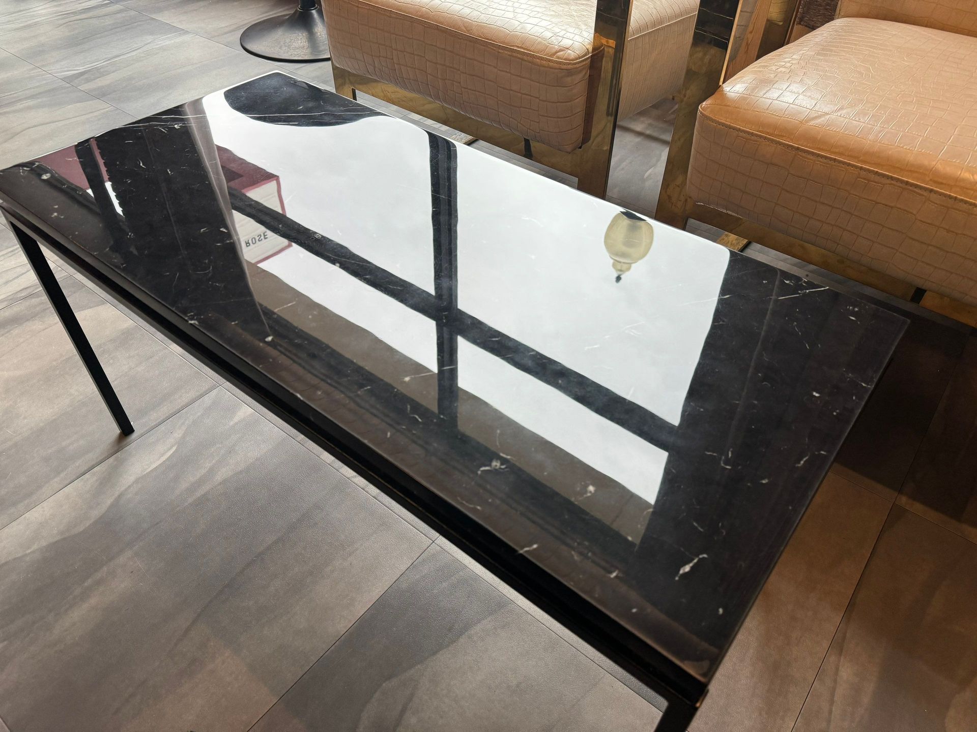 Black glass coffee table reflecting chairs and a bright window in a modern room