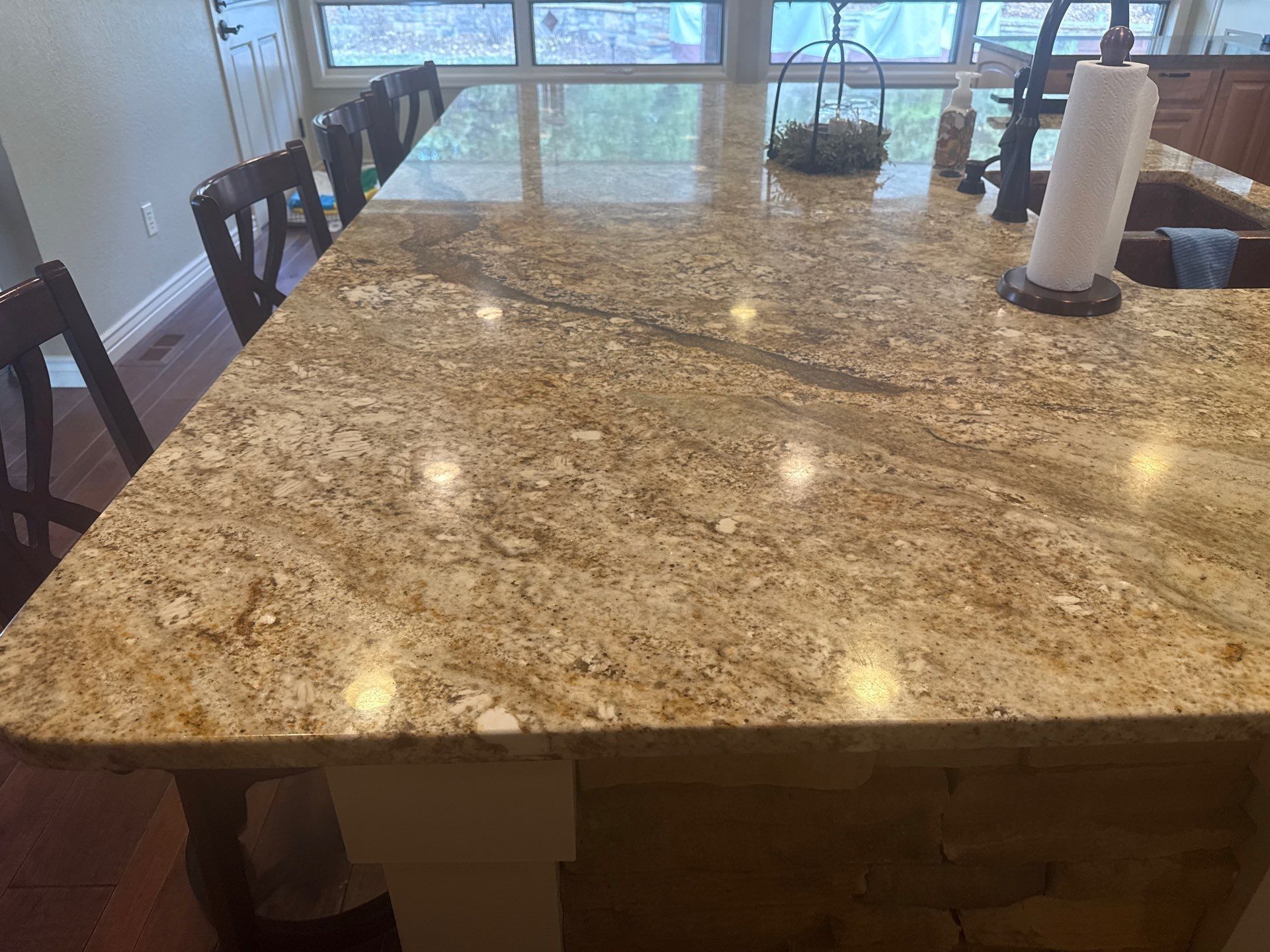 Large granite kitchen island with bar stools and paper towel holder near a bright window