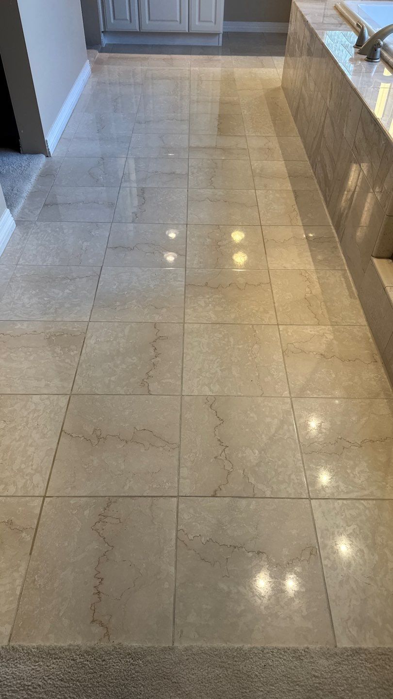 Polished beige stone floor in a hallway, reflecting overhead lights, with a doorway in the background