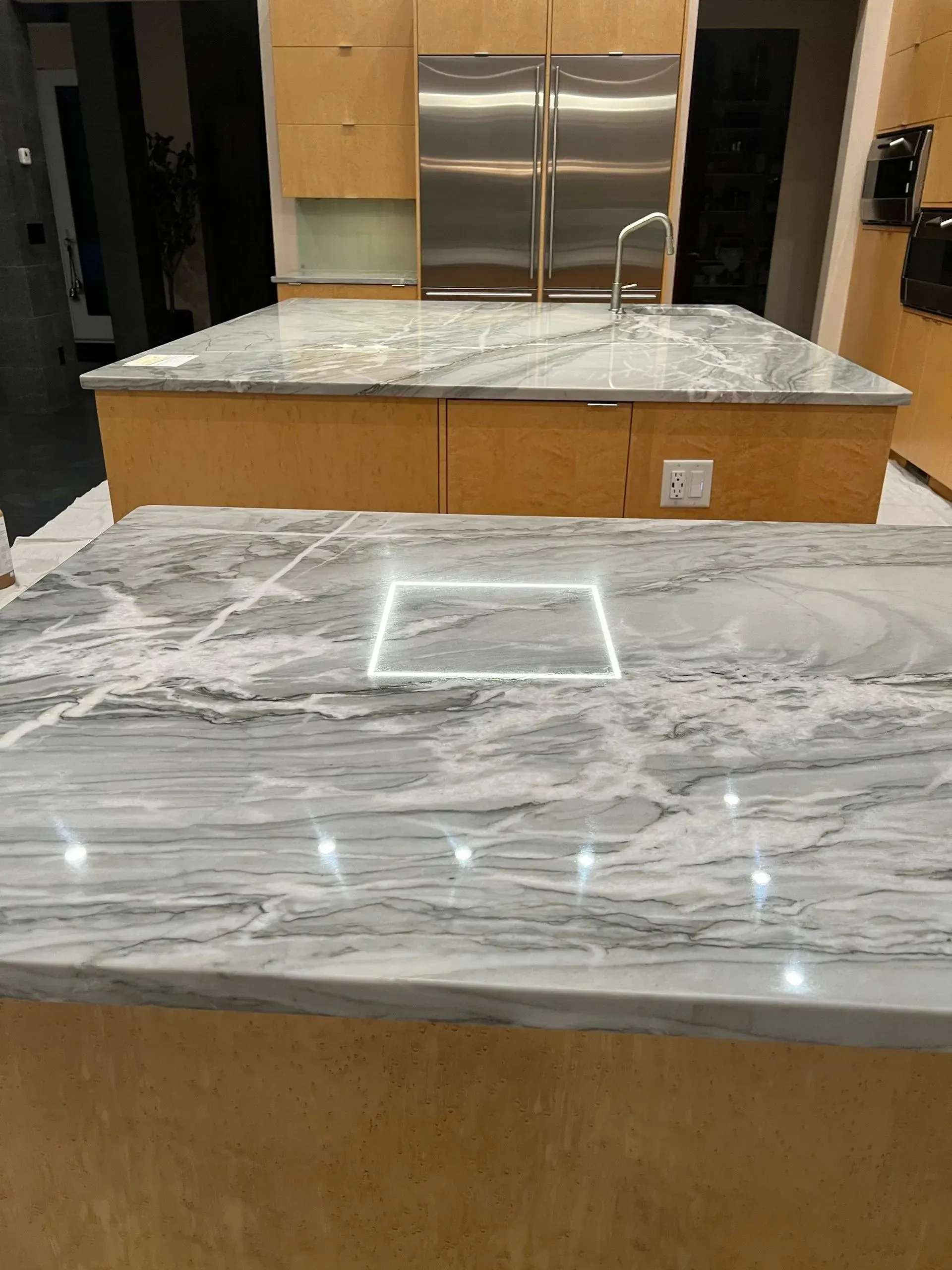 Modern kitchen with marble countertops and a center island, featuring a built-in sink and stainless steel refrigerator.