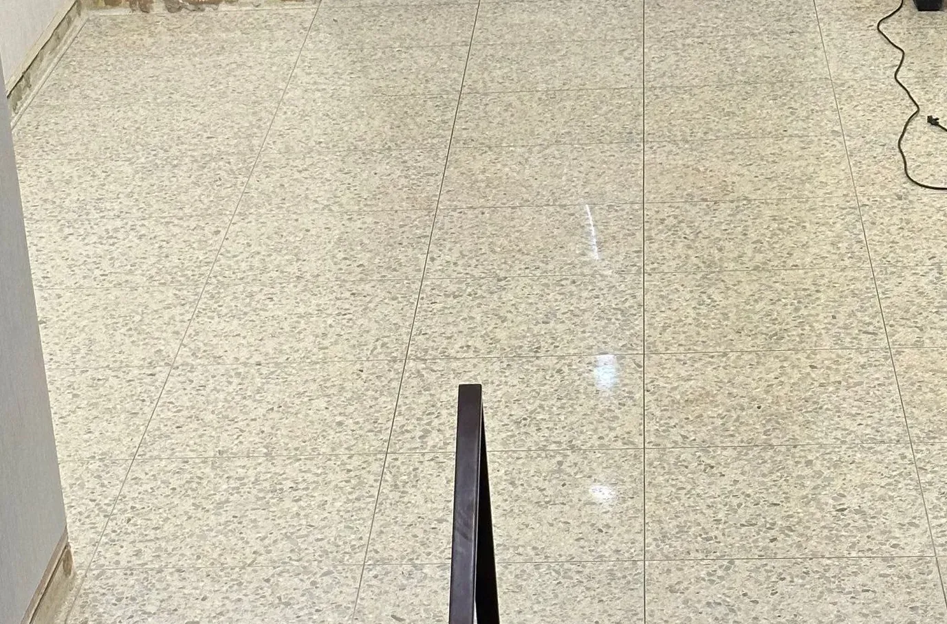 Indoor speckled tile floor with a dark triangular object centered at the bottom edge.