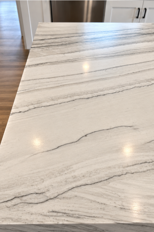 Modern kitchen with a large marble island, warm pendant lights, and glossy white cabinets