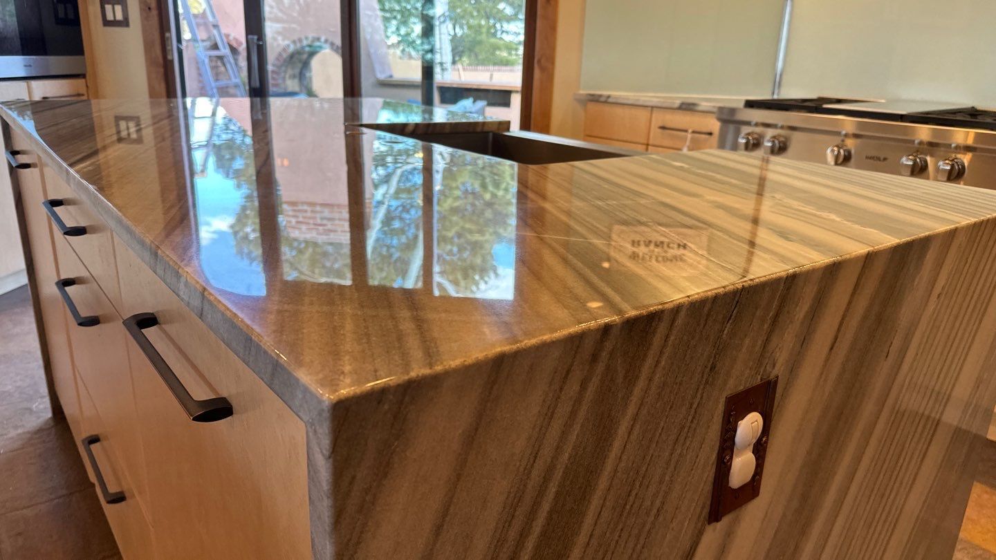 Modern kitchen island with brown wood base and glossy marble countertop, reflecting windows and lights