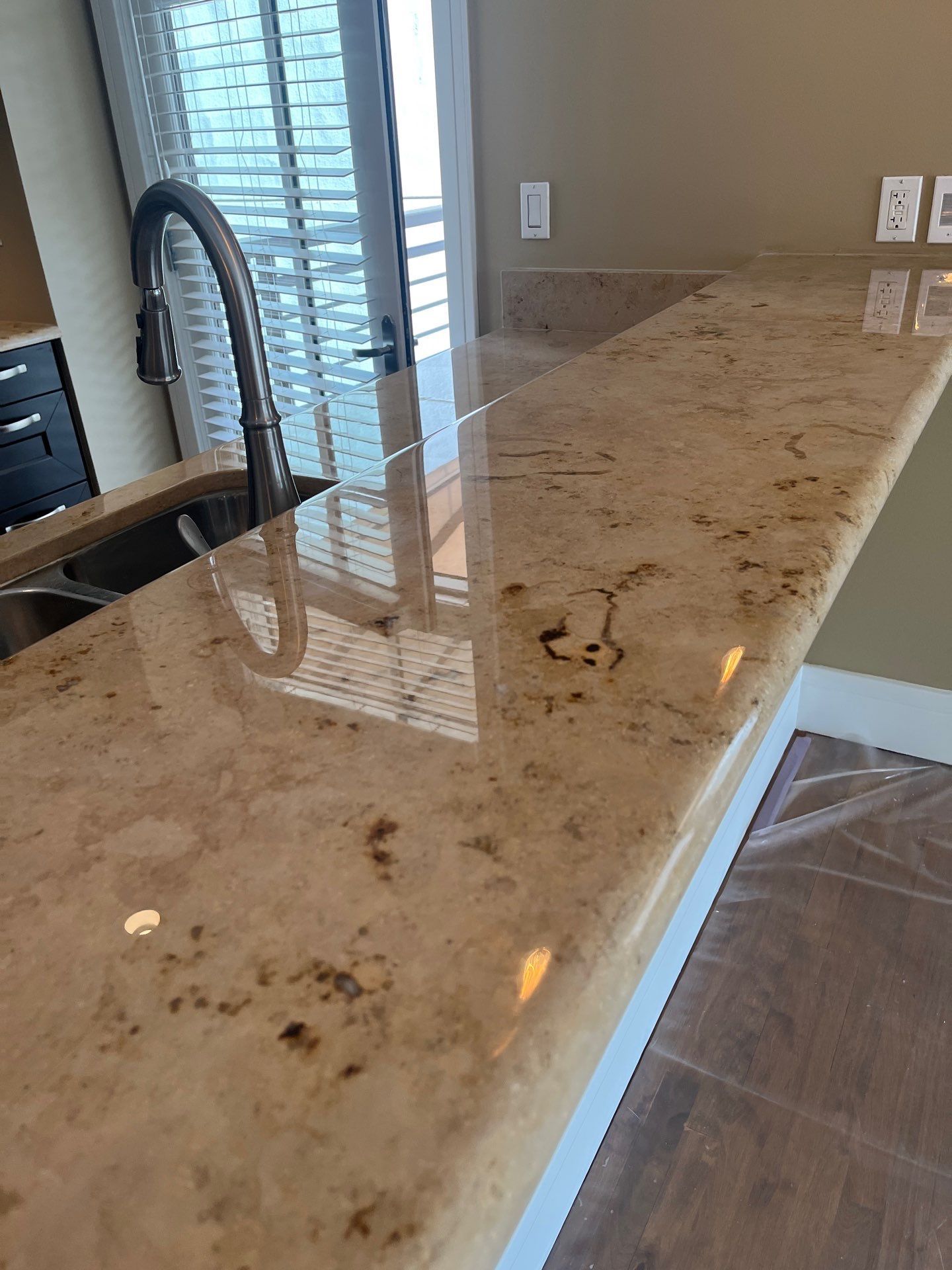 Polished granite countertop with brown and tan speckles. Kitchen setting with a sink, faucet, and window.