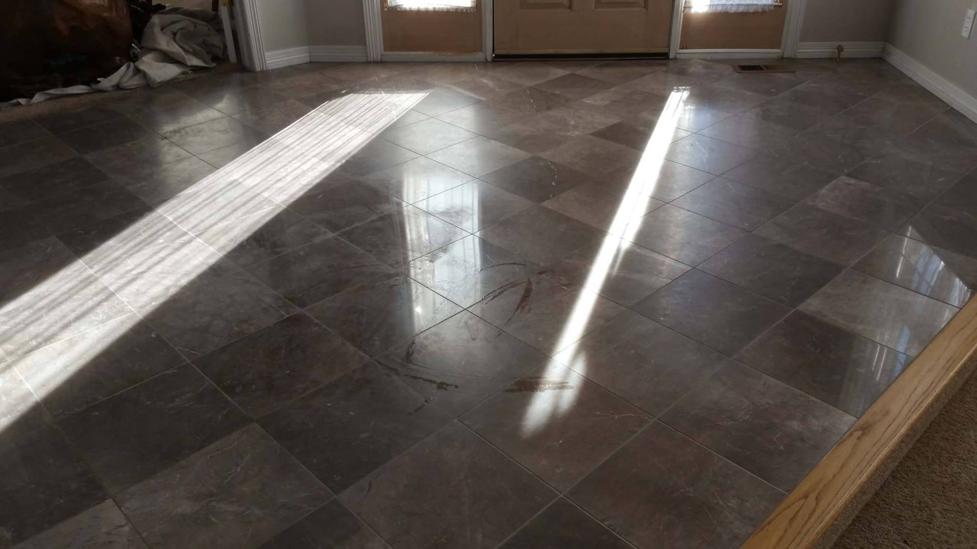 White tiled wall above beige marble baseboard and dark wood floor, with a cardboard box at right edge