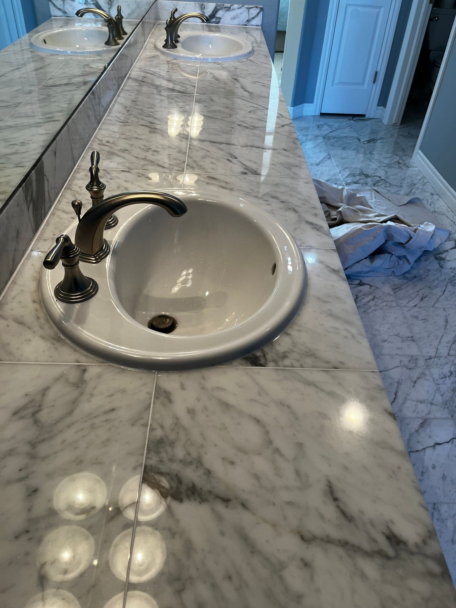 Marble bathroom countertop with two white sinks and bronze faucets, one sink in the foreground.