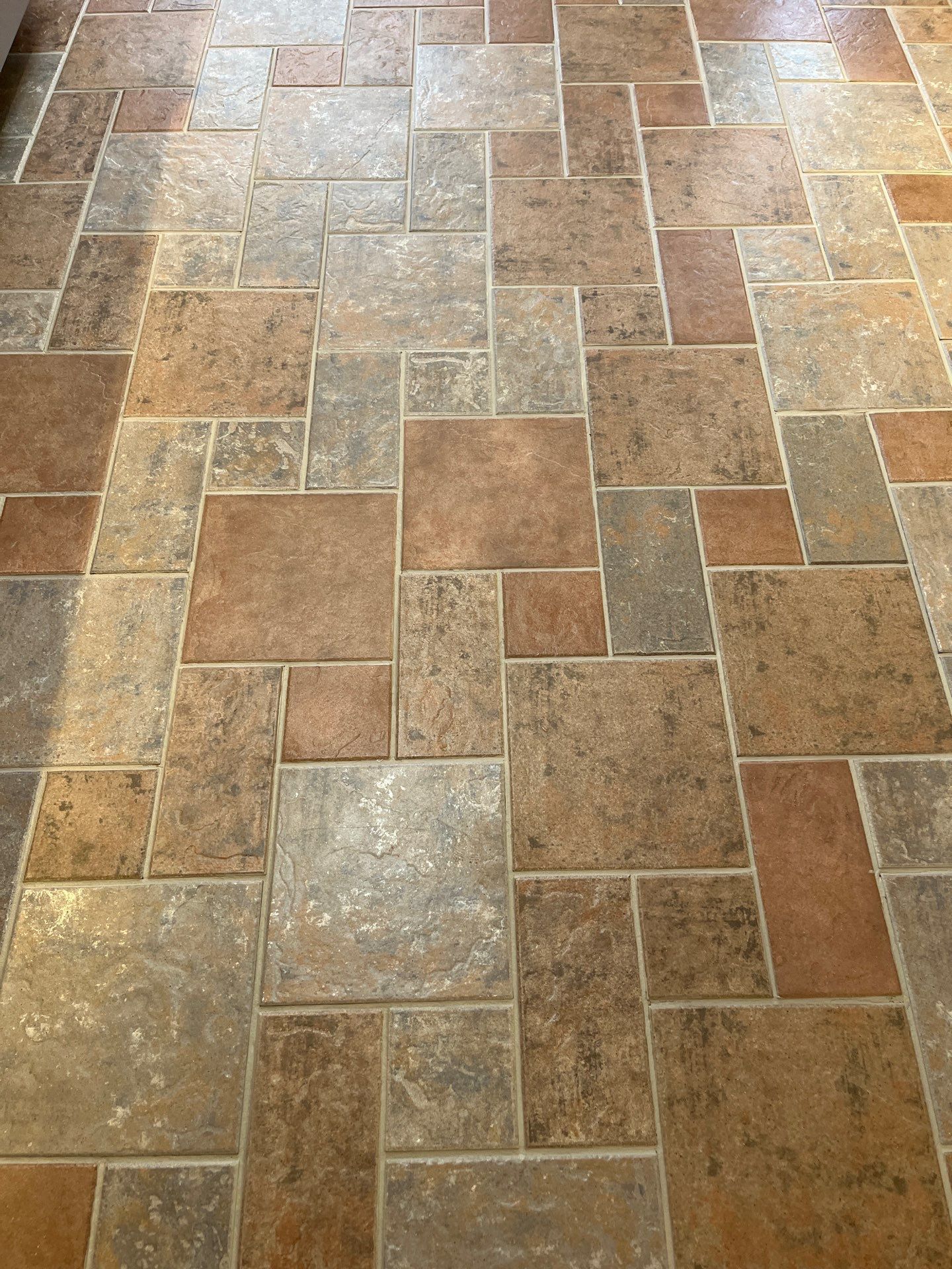 Light wood-look floor tiles leading to a doorway, with dark cabinets on the right and a person’s leg at left.