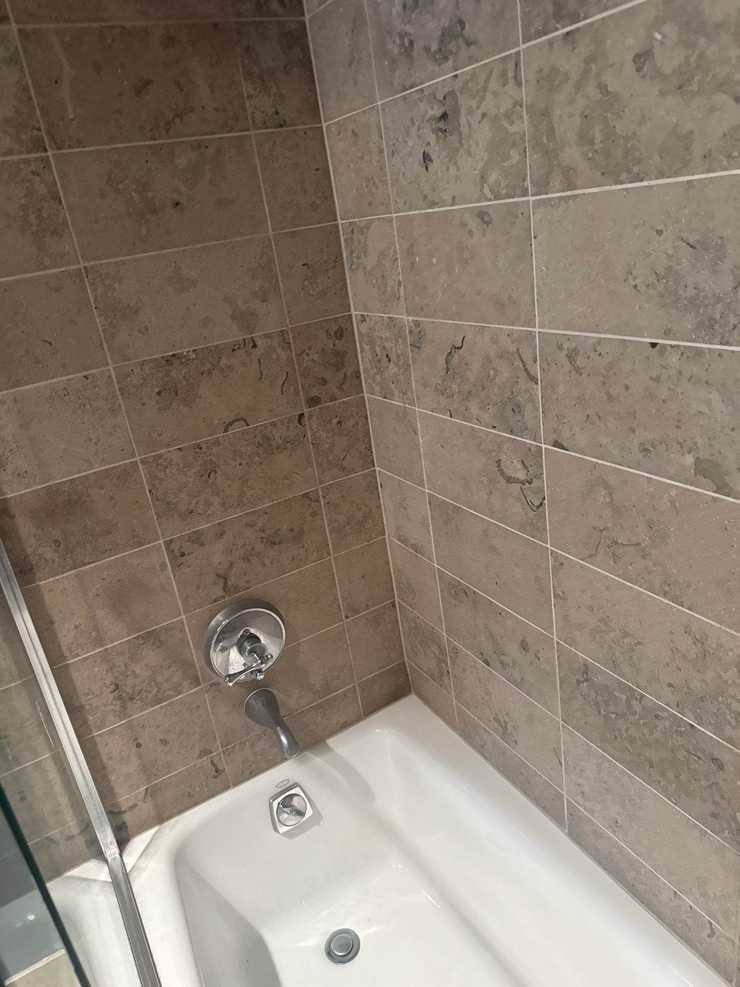 Bathroom shower stall with beige tile walls and a shampoo bottle on the ledge.