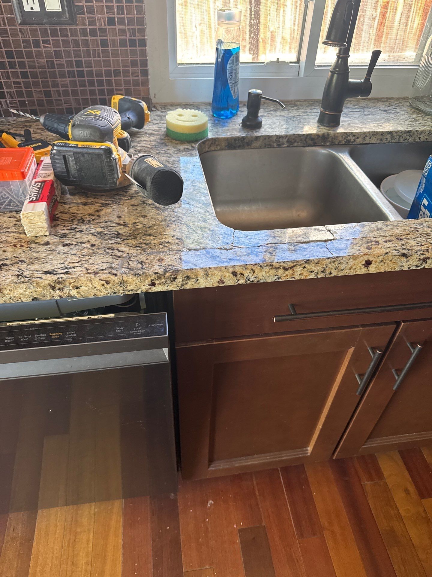 Granite countertop beside a sink, with a marbled brown and white surface and beige tile wall.