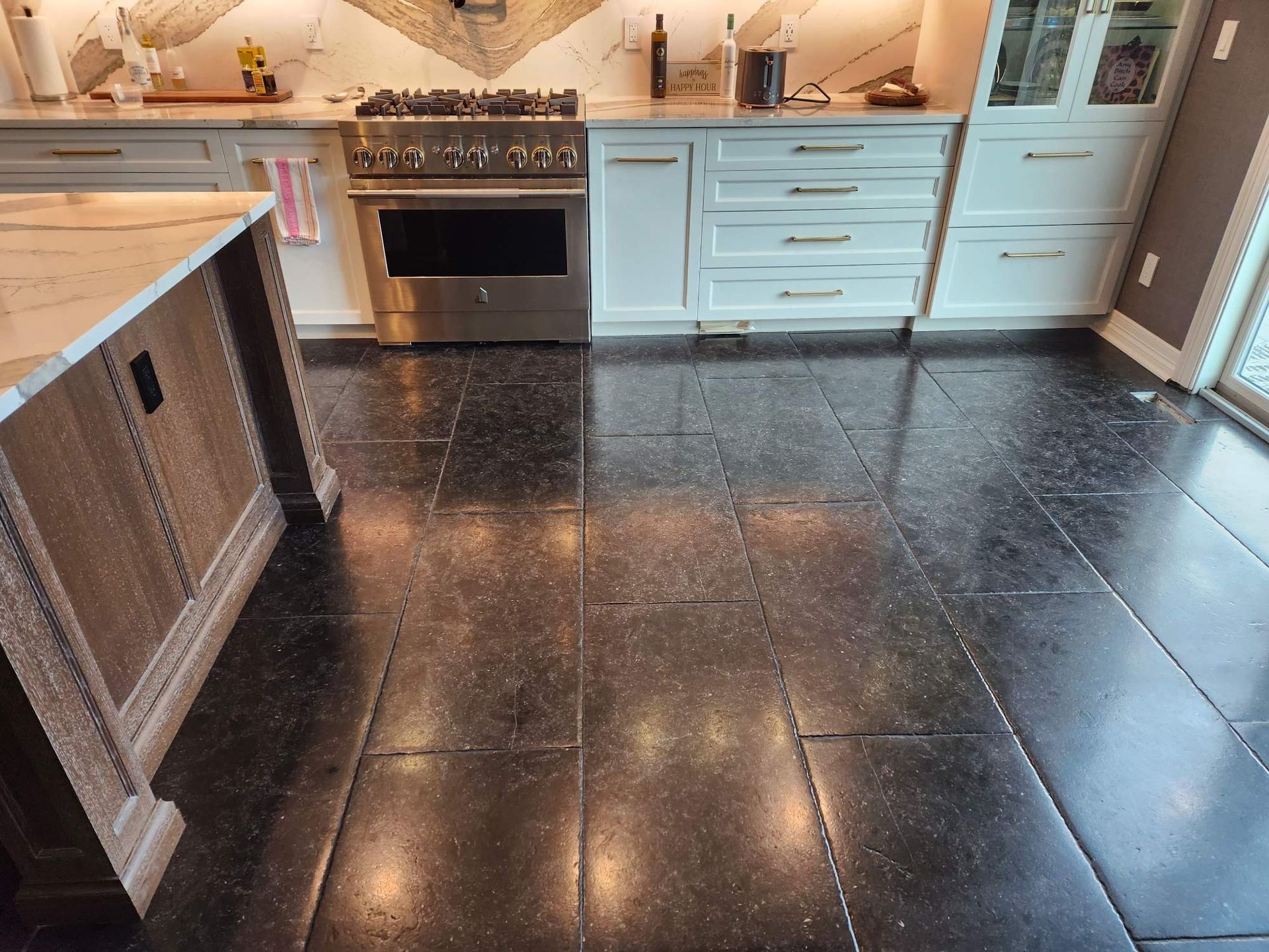 Modern kitchen with dark tile floor, light wood cabinets, and white appliances under warm lighting