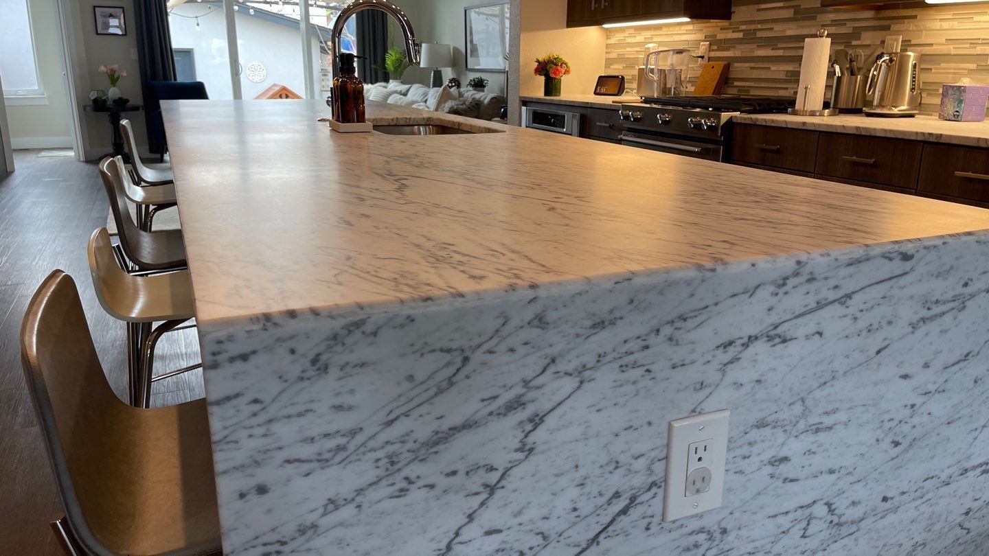 White marble bathroom vanity with a round sink, chrome faucet, and toiletries on a tiled floor area.