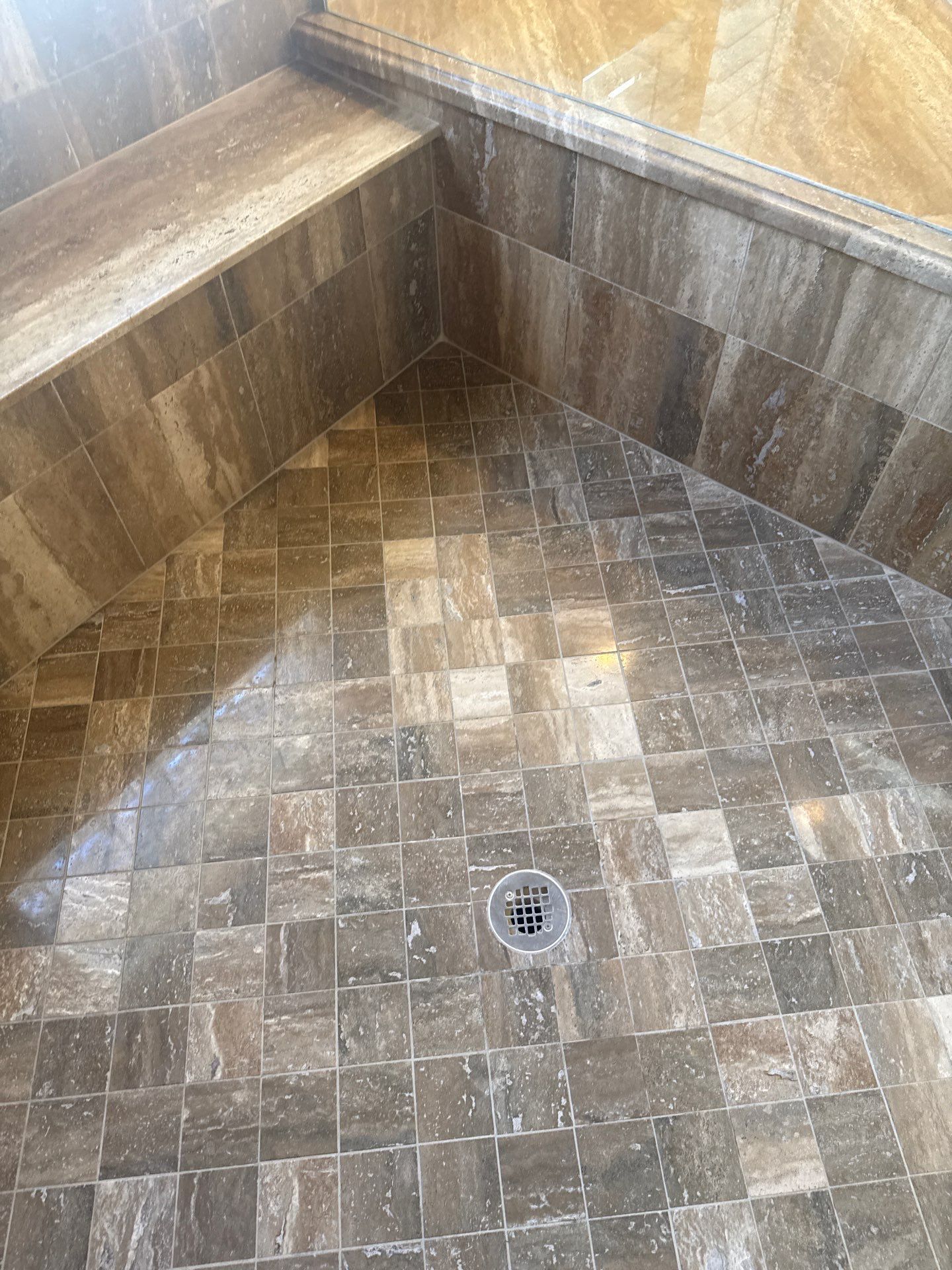 Tiled shower with built-in bench, grab bar, and small floor drain.