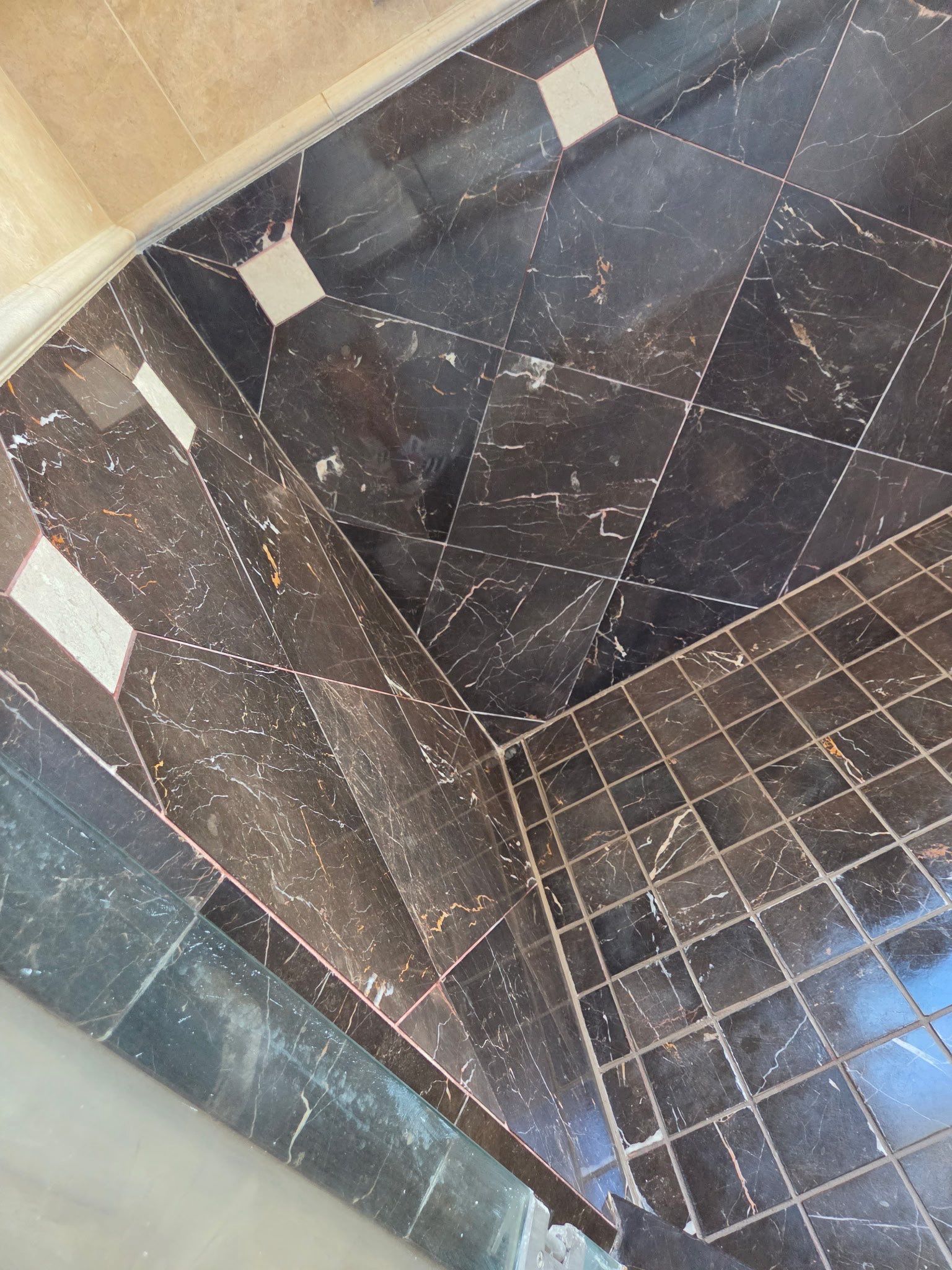 Shower with beige tile, multiple chrome fixtures, and a glass door on the right.